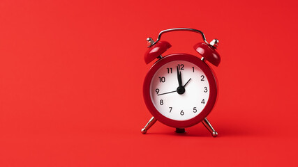A classic red alarm clock stands out boldly against a monochromatic red background.