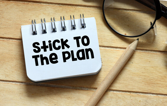 Stick To The Plan words in a small notebook on a wooden table.