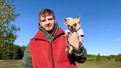 Portrait of happy young man with his Chihuahua dog, hold on hands little puppy on natural...