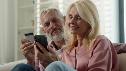Elderly happy Caucasian married couple senior man woman retired make order purchase at online shop using phone pension credit card enjoy easy buying at ecommerce website use electronic bank services - Powered by Adobe