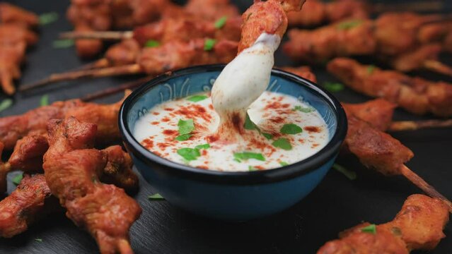 Dipping chicken fillet on skewers in white sauce.