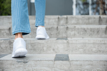 With determination, a woman in sneakers takes on the city stairs, reflecting her relentless progress. Every step symbolizes her commitment to success and ongoing growth. step up