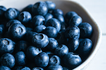 Ceramic white bowl with blueberries on a white background, close-up, summer berries.