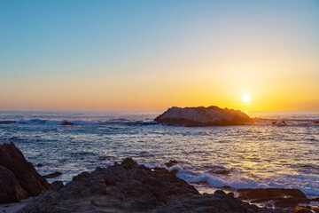 Birds sit on a rock during sunset over sea. Sunset at California with silhouettes of rocks and a sea gull in the distance. Silhouette bird with sunset and sea. Seagulls sit on a rock at sunset