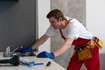 Obraz premium Male plumber repair sink faucet at client home. Man mechanic or repairman fix pipeline at customer kitchen. Good quality plumbing company service. Maintenance and household assistance concept