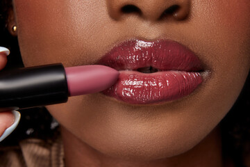 Perfect natural lip makeup. Close up photo of African-American woman applying matte lipstick. Moisturizing with natural gloss lips.