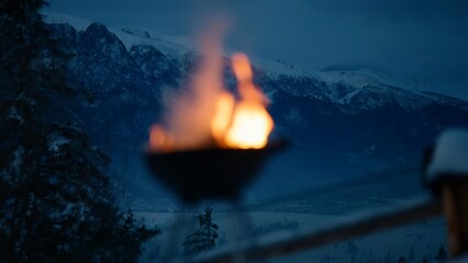  View of a logs burning in a barbecue pot, winter scenic mountains covered with snow in the...