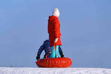 A 10-12 year old girl stands on the top of a snowy hill with a tubing in her hands. Children 10-12...