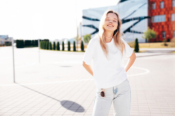 Portrait of beautiful smiling model. Female dressed in summer hipster white T-shirt and jeans. Posing  in the street at sunny day. Funny and positive woman having fun outdoors