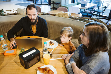 Caucasian family spending time togehter while the father is working on laptop