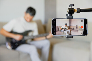 A man records playing guitar on his phone; the mobile phone is mounted on a tripod to record video. Online lessons, music training, education. Personal music blog about electric guitar