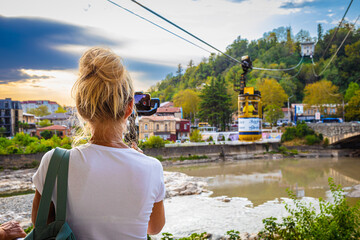 A girl blogger uses a mobile phone to take a photo of the cable car in Kutaisi. Selective focus. Georgia