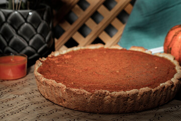 pumpkin pie round shape, dark background, musical notes sheet baking paper, decorative small orange pumpkin vegetable, kitchen textile, rustic style