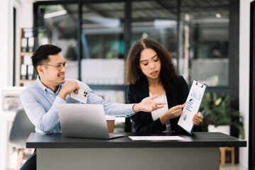 Two Asian businesswoman and man discuss investment projec with tablet laptop computer.