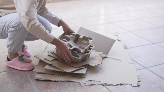 Woman sorting cardboard boxes for garbage during the day on the veranda