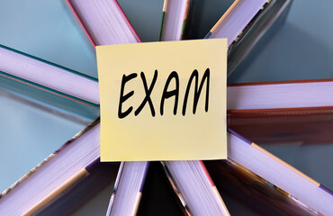 EXAM - word on a yellow piece of paper on the background of books