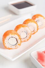 Fresh healthy Philadelphia roll type of sushi made with smoked or raw salmon, cream cheese, with boiled rice and nori seaweed served on plate with marinated ginger and soy sauce on white wooden table