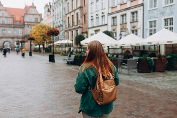 Back view of a young tourist. Autumn casual fashion street style. 30s alone woman walking on the...
