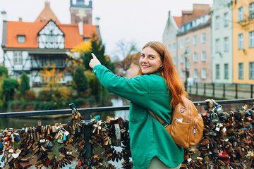 Young pretty woman with backpack standing and pointing to object on copy space, rear view against the Millers' Guild house and the Radunia Canal in Gdansk,