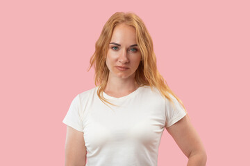 Portrait of serious young woman with ginger wavy hair and green eyes looking in the camera. Pink background. Beautiful confident woman