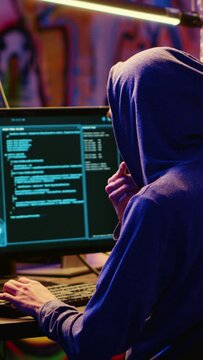 Vertical video Hacker in graffiti painted hideaway base writing lines of code on computer, developing malware that get past security systems. Rogue programmer uses PC in bunker, running hacking script
