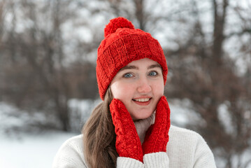 Portrait of young pretty woman in woolen clothes outdoors, cold weather. Smiling girl in knitted red hat and mittens, winter park