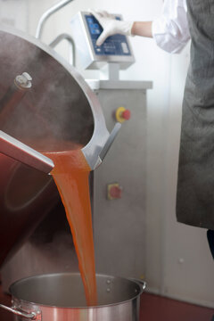 Factory worker using computer controlled machinery pouring tomato sauce into a pan
