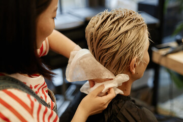 Close up of hairstylist working with male client in beauty salon and using tissue
