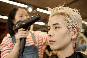 Close up portrait of young Asian man in beauty salon with hairstylist drying hair, copy space