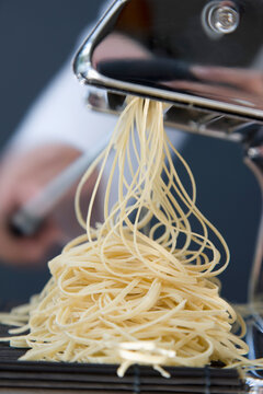 Heap of fresh tagliolini coming out of a pasta maker with hand turning the handle
