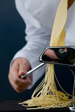 Close up of a chef hand turning the handle of a pasta maker with tagliolini coming out
