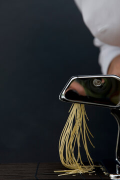 Close up of a chef hand turning the handle of a pasta maker with tagliolini coming out
