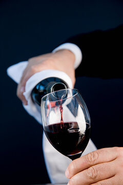 Close up of a waiter hands holding a bottle and pouring red wine in a glass
