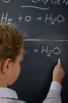 Back view of a school boy writing on a blackboard
