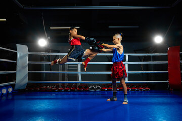 Fototapeta na wymiar Two serious boys, kids, kickboxers, professional martial arts sportsmen performing kicks, training on ring at gym.