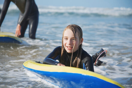 Smiling and wet girl in the sea holding on to her surfboard
