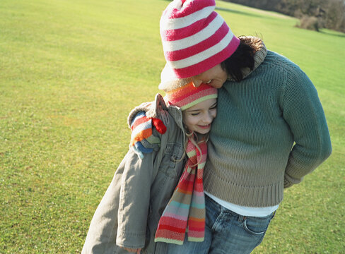 Woman and girl standing in a field hugging
