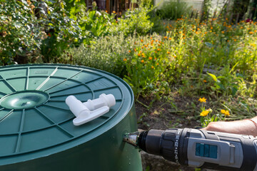 Gardener mounts a faucet on a rainwater collection barrel for watering the garden.