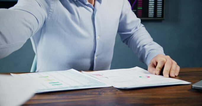 Male trader hands over papers of crypto global market statistics at wooden table in office. Market broker tries to explain cryptocurrency operation