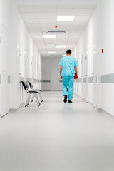 A tall male doctor with a beard walks along the hospital corridor with folder of documents