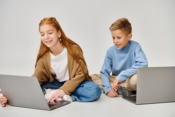 joyous little boy looking at laptop of his preteen friend and smiling cheerfully, fashion concept