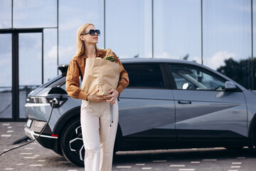Woman with food shopping bags charging electric car