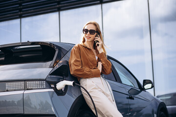 Woman talking on the phone by her electric car