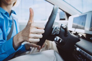 Woman sitting in electric car and showing thumbs up sign - obrazy, fototapety, plakaty