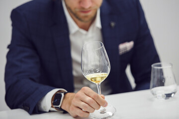 European wine enthusiast evaluating white wine at wine tasting based color rating, close up faceless shot.