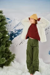 Gordijnen cheerful girl in stylish winter attire posing with hands behind head and looking away, fashion © LIGHTFIELD STUDIOS