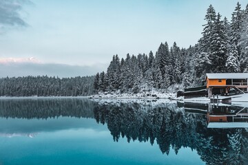 House on the shore of a lake against a forest covered with snow in winter