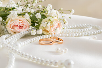 Two gold wedding rings and gorgeous pearl beads against the background of a bouquet with roses on a beige satin background. Front view. postcard.