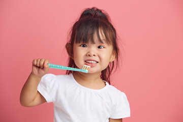 Cheerful little asian girl brushes teeth, has brilliant smile, morning daily hygiene, poses with...