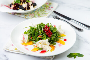 arugula salad with peach slices and red berries on a white plate top view
